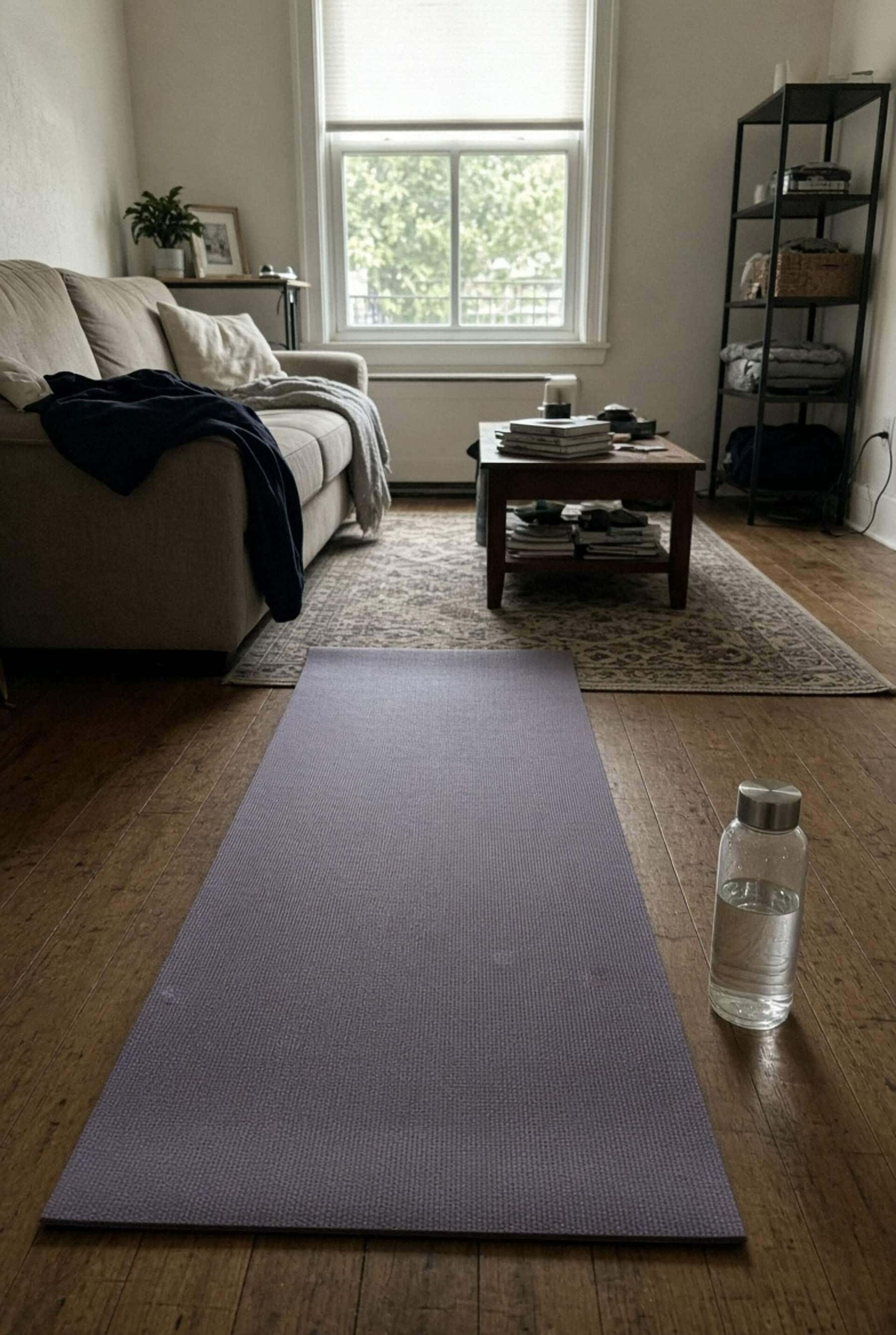 A yoga mat laid out on a timber floor in a living room with a water bottle