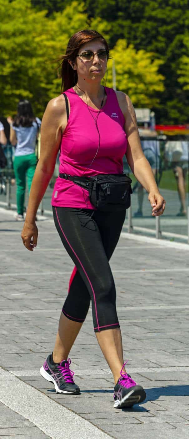 A woman in a pink top and leggings walking briskly along a promenade